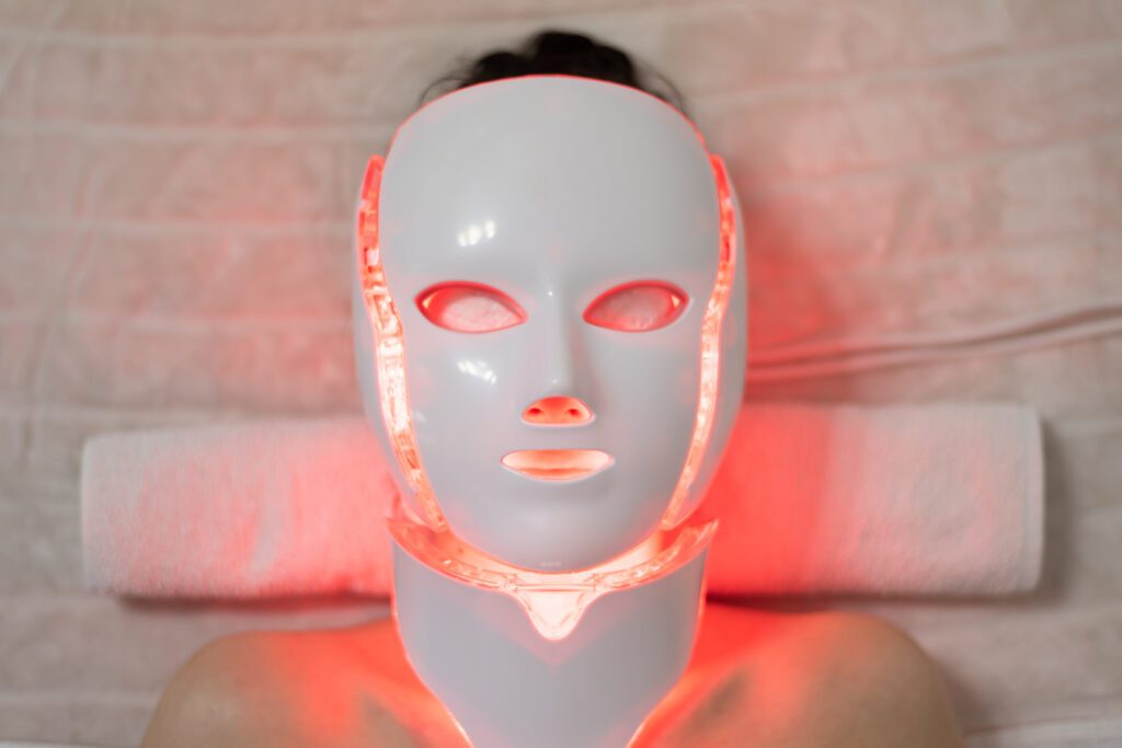 Woman with led light therapy facial and neck beauty mask photon therapy. Home skincare and me time concept